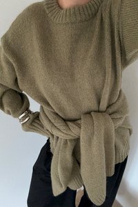 Oliwkowy, dziany sweter z szerokim dekoltem i luźnym krojem. W pasie związany węzłem przypominającym pasek, z prążkowanymi mankietami i dołem.