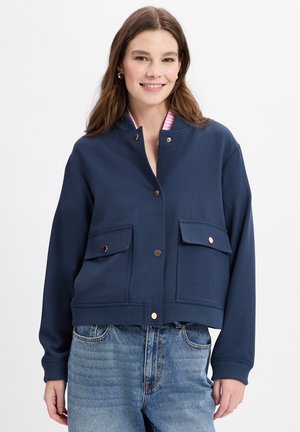 Marineblaue, kurz geschnittene Jacke mit rundem Kragen, zwei vorderen Taschen und Knöpfen in Goldoptik. Innenfutter mit Streifenmuster sorgt für einen kontrastierenden Akzent.