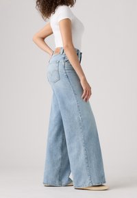 Ljusblå vida jeans med hög midja, tillverkade av denim. Har en klassisk femfickdesign och en brun läderlogotyp på baksidan.