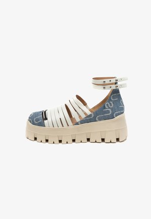 Massieve platformsandaal met witte leren bandjes, dubbele enkelgesp, blauwe denimhak en dikke beige zool met diepe profielzolen, zijaanzicht.
