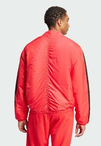 Red nylon bomber jacket with black side stripes, elastic hem, and gathered back seam. Worn with matching red sweatpants.
