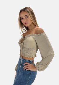 Beige off-shoulder crop top med knyte foran, smock-detaljer og lange ærmer; kombineret med en højtaljet denim nederdel.