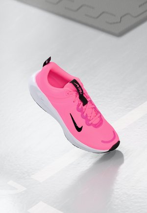 Baskets de course Nike en rose vif, avec un swoosh noir et des accents. Présente une texture lisse et une semelle blanche rembourrée. Les lacets sont exposés.