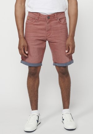 Rode denim shorts met opgerolde blauwe zomen, frontzakken en subtiele vervaging, gecombineerd met witte sneakers en crew-sokken.