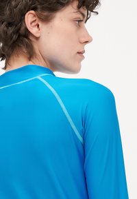 Top azul de manga longa feito de um tecido liso e elástico. Apresenta um colarinho redondo e costuras em azul claro em contraste ao longo das costuras.