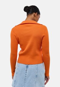 Pull en rib d'orange avec un col, design ajusté et manches longues, associé à une jupe en denim clair. La texture est lisse et extensible.