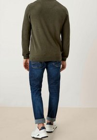 Un pull en tricot vert olive associé à un jean en denim bleu foncé avec revers et des baskets blanches avec des accents navy, vu de dos.