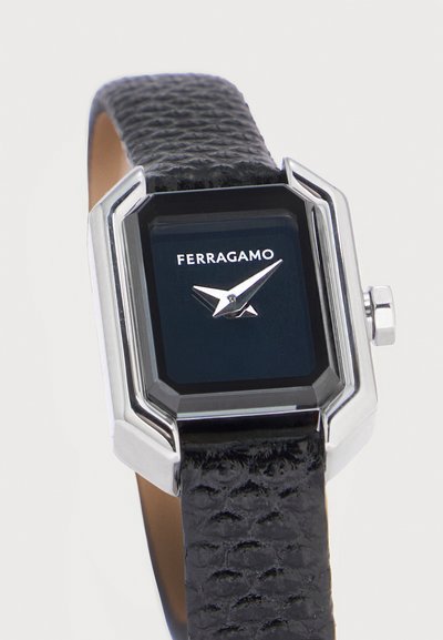 Montre Ferragamo avec bracelet en cuir noir texturé, boîtier rectangulaire en argent et cadran noir affichant le nom de la marque ainsi que les aiguilles des heures et des minutes en argent.