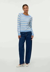 Prugasta pulover v svetlo modri in beli barvi iz bombaža, s čolnovim izrezom. Kombiniran z temno modrimi širokimi hlačami in belimi natikači.