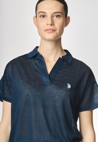 Polo shirt blu navy realizzato in tessuto leggero e leggermente trasparente, con scollatura a V, maniche corte e logo ricamato sul petto.