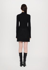 Maglietta nera a maniche lunghe abbinata a una mini gonna nera con texture. Indossata con stivali neri con tacco alti fino al ginocchio, che mostrano una silhouette slanciata.