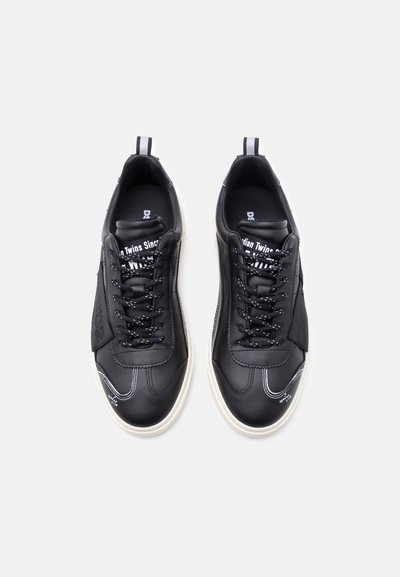 Μαύρα αθλητικά παπούτσια χαμηλού ύψους με λευκή σόλα, μαύρα κορδόνια, λευκές ραφές και θηλιές για να τα τραβάτε, σε ένα απλό ανοιχτό φόντο.