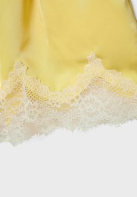 Tissu satin jaune avec une bordure en dentelle florale blanche complexe le long du bord, mettant en valeur la texture et un travail délicat.
