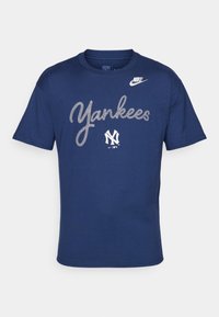 Camiseta de algodón azul marino con el texto "Yankees" en una fuente curva blanca y un pequeño logo blanco en el hombro izquierdo. Cuello redondo, mangas cortas.