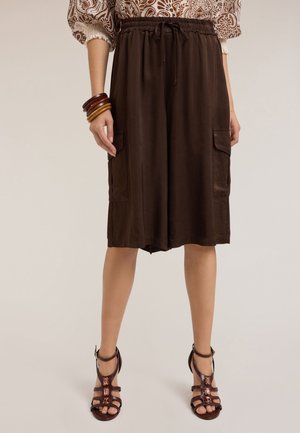 Bermudas marrones hasta la rodilla, hechas de un tejido ligero, con dos bolsillos laterales, cintura elástica con cordón, combinadas con sandalias marrones de tiras.
