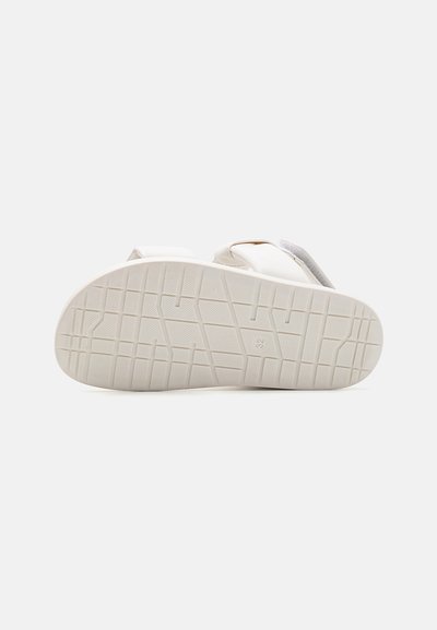 Sandalia blanca con suela de goma texturizada, que presenta dos correas anchas y un diseño minimalista. La suela tiene un patrón de rejilla para mayor tracción.