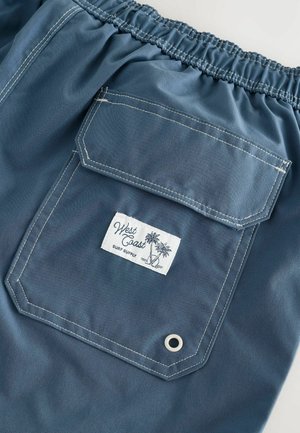 Modré šortky s elastickým pasem, s velkou zadní kapsou, bílou nášivkou s designem palmy a kontrastním šitím.