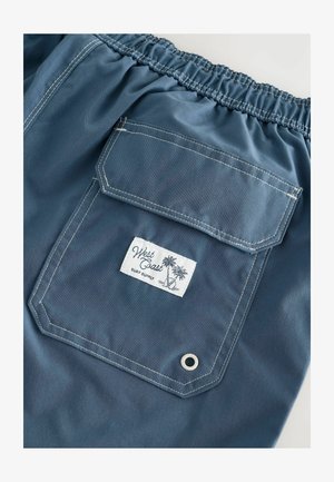 Blaue Shorts mit elastischem Bund, ausgestattet mit einer großen Gesäßtasche, weißem Etikett mit Palmenmotiv und kontrastierenden Nähten.