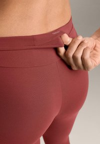 Bordové legíny z pružnej látky s vysokým pásom a nenápadným logom na zadnej strane. Hladká textúra bez viditeľných vzorov.