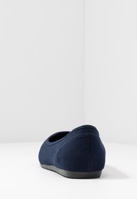 Chaussure slip-on en daim bleu marine avec un dos texturé, une forme arrondie et une semelle en caoutchouc noire. Présente des coutures contrastées le long des bords.