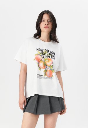 White cotton t-shirt with short sleeves, featuring a colorful apple graphic and text. Paired with a grey pleated skirt.