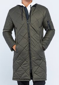 Lang, olivengrøn quiltet frakke med lynlås foran, hætte og lommer. Har et diamantmønster og snørre til justering.