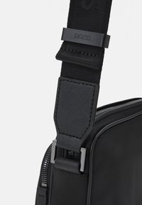 Borsa a spalla nera in materiale sintetico testurizzato, con zip in metallo e tracolla regolabile, caratterizzata dal logo "BOSS" in rilievo e da un design elegante.