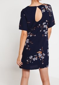 Robe bleu marine avec des manches courtes, motif floral gris et rouille, et un détail en fente au dos. Tissu lisse et coupe décontractée.
