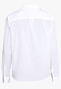 Vit långärmad skjorta i lätt, texturerad tyg. Har en klassisk krage och knappade ärmslut. Enfärgad rygg utan ytterligare detaljer.