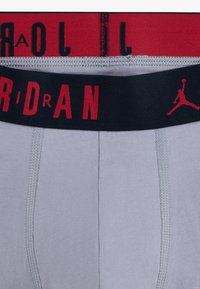 Boxer in cotone grigio con un elastico nero e rosso, con testo "JORDAN" e logo. Texture liscia, design semplice.