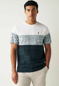 T-shirt med korte ærmer, der har et hvidt topanel, grå og mørk navy striber samt et lille sort logo på brystet; lavet af struktureret stof.