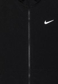 Čierna zipsová bunda vyrobená z mäkkej tkaniny, s bielym logom Nike na ľavej hrudi a výrazným centrálnym zipsom.
