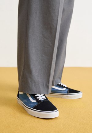 Sneakersy Vans z czarnymi, niebieskimi i białymi akcentami; materiał zamszowy i płócienny; płaska biała podeszwa; sznurówki i kontrastowe detale przeszyć.