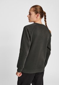 Mörkgrön bomulls-tröja med rund halsringning, raglanärmar och avslappnad passform. Enkelt mönster med ribbade ärmslut och nederkant.