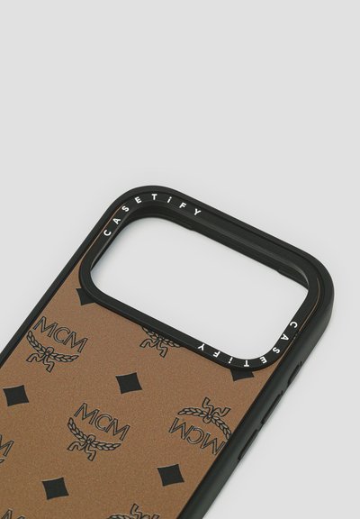 Custodia per telefono marrone con bordo nero, con loghi MCM in rilievo e motivi a diamante. Il nome del marchio "CASETiFY" è inciso sul bordo.