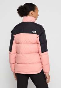 Pufferjacka med svart överdel och rosa nederdel. Tillverkad av glansigt material med hög krage, horisontell sömnad och logotypdetalj.