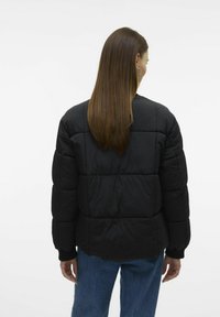 Veste doudoune noire avec des sections matelassées, des épaules arrondies et des poignets côtelés. Texture lisse et design minimaliste ; convient pour une tenue décontractée.