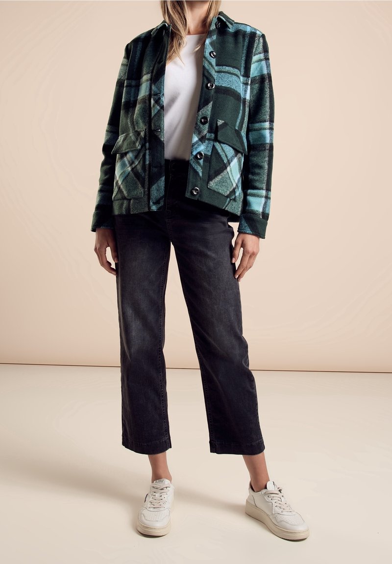 Zielona kratkowana kurtka z niebieskimi akcentami, dwoma przednimi kieszeniami, czarnymi prostymi dżinsami i białymi trampkami. Gładka tekstura z zapięciem na guziki.