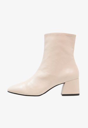 Beige läderankelboot med spetsig tå och klack. Slät textur, minimal design och en diskret logotyp på sidan.