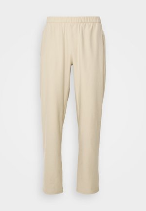 Pantaloni beige con cintura elastica, dotati di tasche laterali, gamba affusolata, tessuto leggero e morbido. Nessun motivo o decorazione visibile.