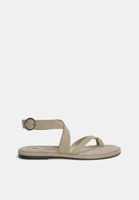 Beige suede sandaal met een platte zool, voorzien van kruislings banden en een gespen enkelsluits. Gladde textuur en minimalistisch ontwerp.
