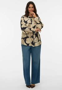 Chemise beige à manches longues avec un grand motif floral noir, associée à un jean en denim bleu ample et des chaussures à bout pointu marron.