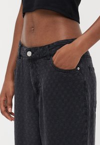 Zwarte geruite jeans van textuurstof, met een voorzak en details van zilveren knopen. Close-up van de taille en handplaatsing.