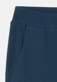 Dark blue textured fabric with a ribbed elastic waistband and side pocket seam detail on a garment.