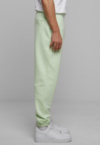 Pantalones de chándal verde claro con pierna ajustada, puños elásticos y un bolsillo trasero. Combinados con zapatillas blancas, que muestran un aspecto limpio y casual.