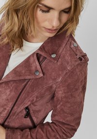 Suede violetinė striukė su užtrauktuku priekyje, spaudžiamomis sagomis ir asimetrišku apykakle. Lygi tekstūra su matomomis siūlėmis.