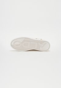 Sole di sneaker bianca con un motivo di grip testurizzato. Presenta una forma arrotondata e un testo di marca prominente sul lato. Materiale di gomma liscia.