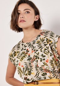 Top de lino de manga corta con un patrón botánico en verde, amarillo y rojo sobre un fondo crema. Cuello redondo y corte relajado.