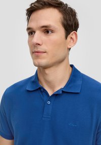 Polo shirt blu in cotone con colletto a due bottoni e una texture morbida. Presenta un piccolo logo ricamato sul lato sinistro del petto.