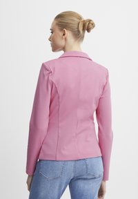 Roze getailleerde blazer met een geknikte kraag en lange mouwen, voorzien van een gladde textuur en gestructureerde naden, gecombineerd met lichtblauwe jeans.